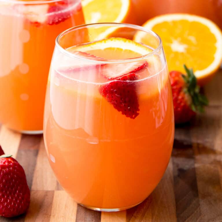 square image of orange strawberry rose sangria on a cutting board in a stemless wine glass