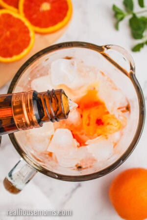 Cointreau being poured into a blender with ice, orange kool-aid, and orange juice