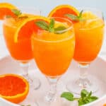 square image of three orange vodka slushes with orange slices and mint for garnish