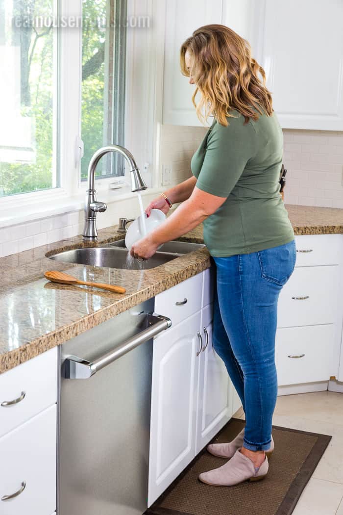 woman standing at a sink rinsing dishes next to a Beko dishwasher