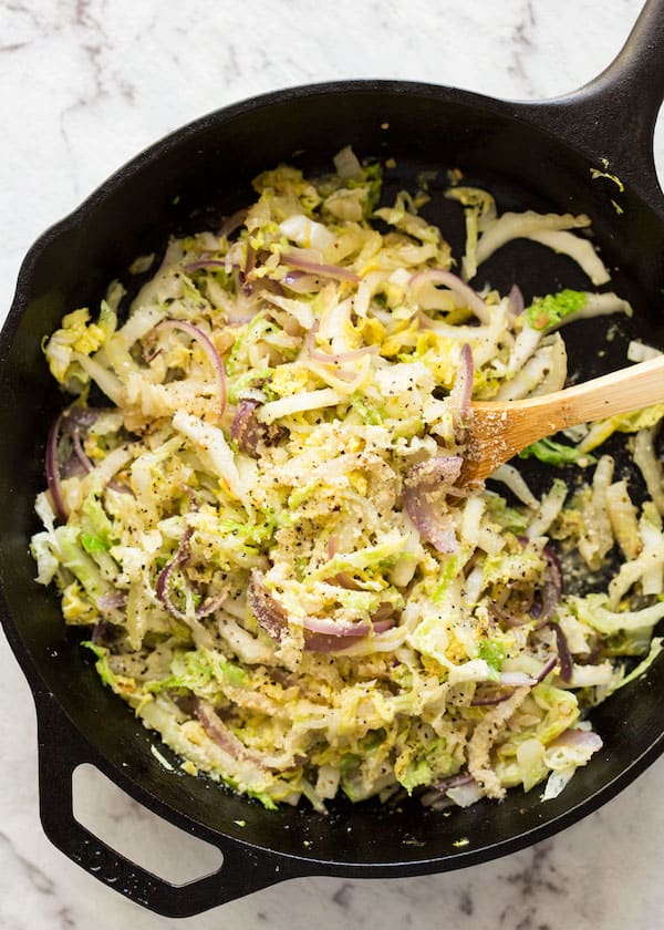 Overhead shot of Parmesan Garlic Cabbage in a cast iron skillet with a wooden spoon for serving