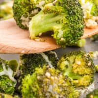 parmesan roasted broccoli on a wooden spatula over the baking sheet with recipe name at the bottom