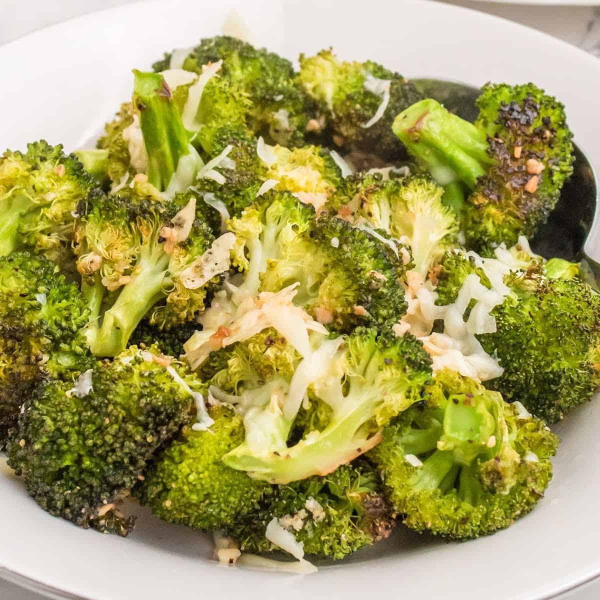 square image of parmesan roasted broccoli in a serving bowl with a spoon