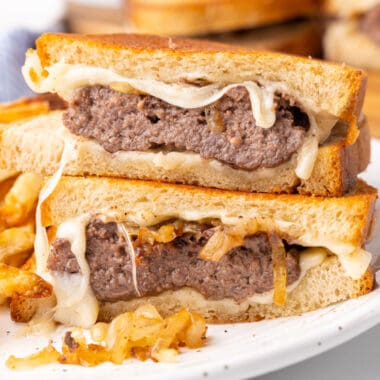 square image of patty melt halves stacked on each on a plate with with fries