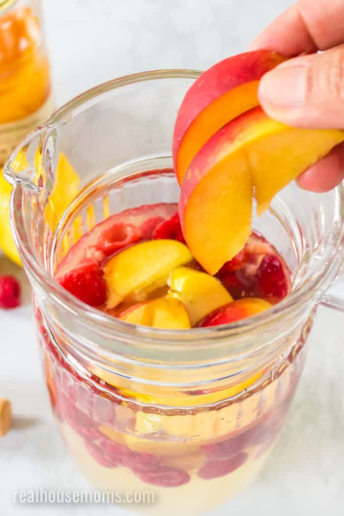 fruit being added to a pitcher of sangria