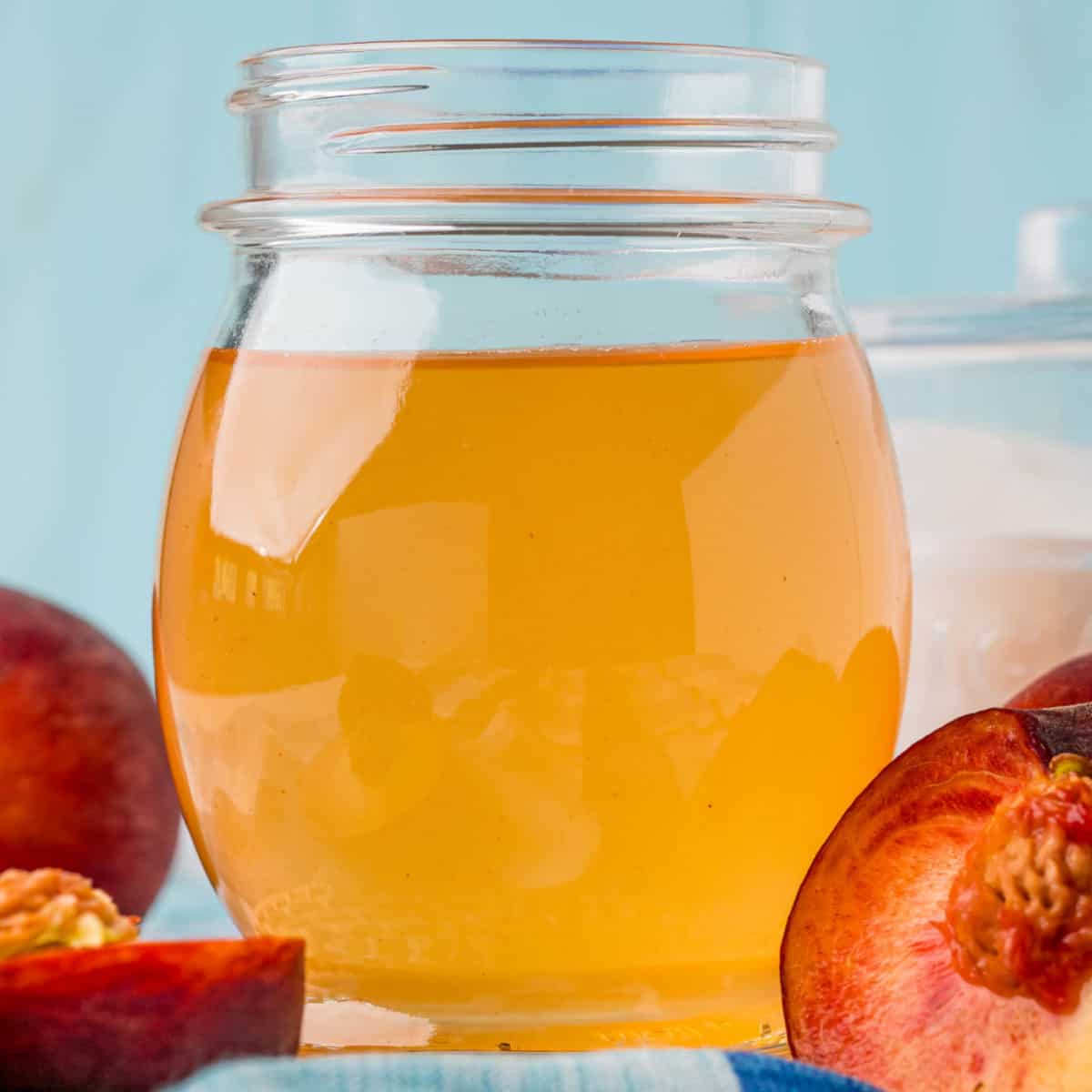 square image of peach simple syrup in a jar next to peaches