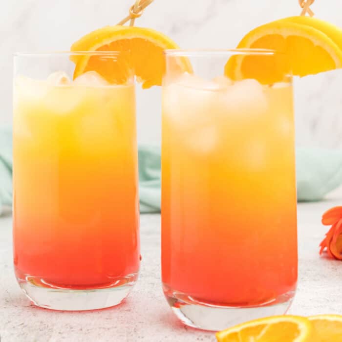 square image of two glasses of peaches and cream cocktail wit an orange wedge
