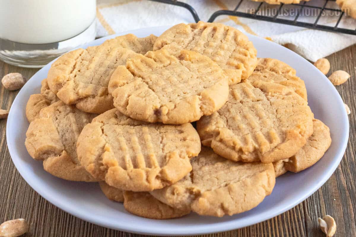 side view of peanut butter cookies on a white plate next to a glass of milk