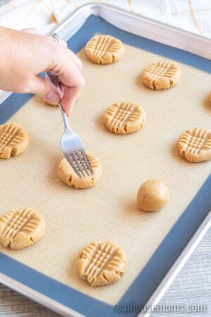 fork tines being pressed into a ball of peanut butter cookie dough to make the crisscross shape