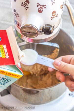 milk being measured to pour into peanut butter cookie dough base in a stand mixer bowl