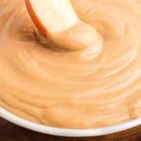 an apple sliced being dippedin to a bowl of peanut butter dip with recipe name at the bottom