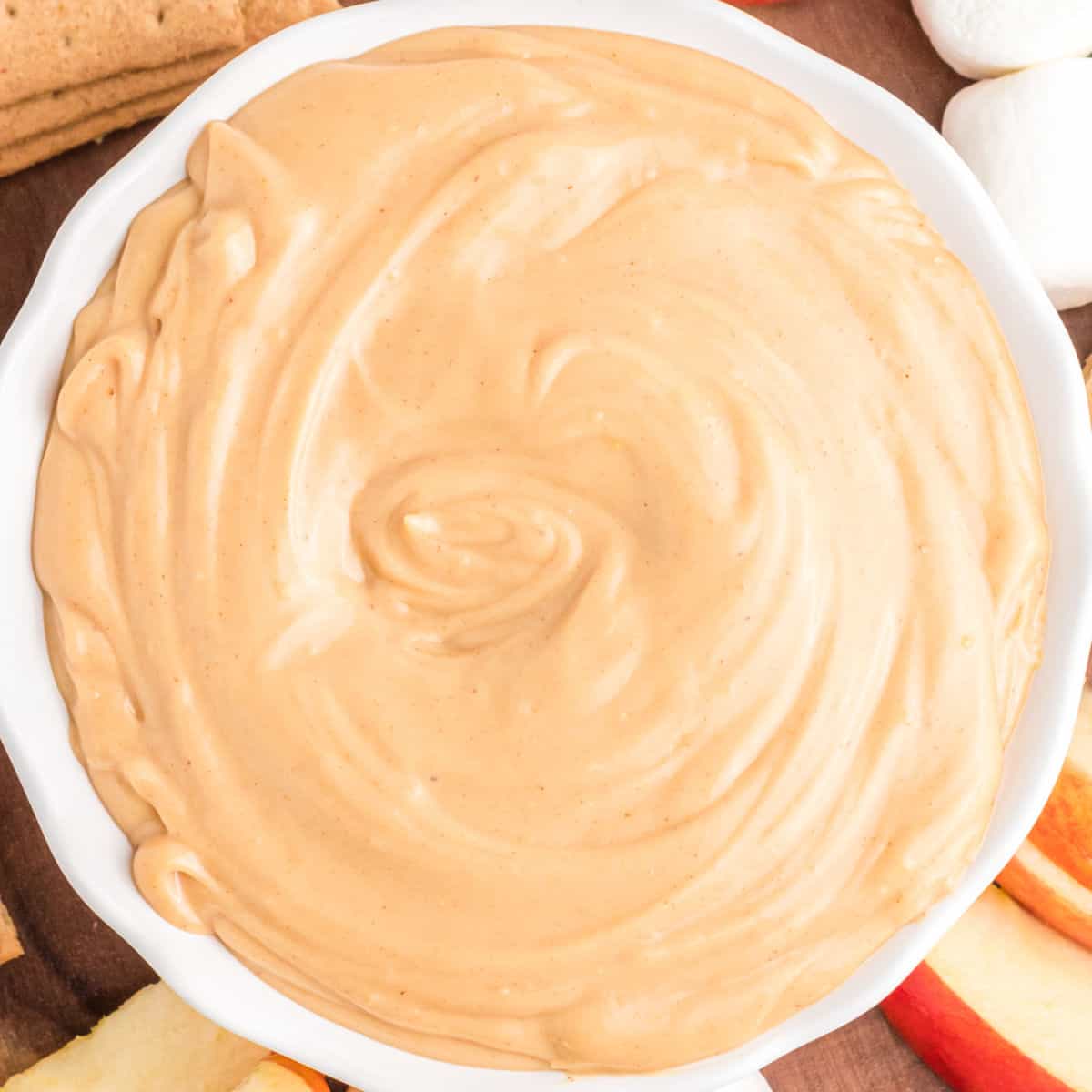 square image of peanut butter dip in a white bowl on a board with food for dipping