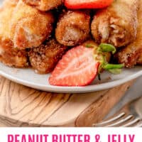 peanut butter & jelly french toast roll ups and halved strawberries piled on a plate with recipe name at the bottom