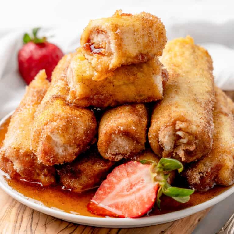 square image of peanut butter & jelly french toast roll ups piled on a plate with one cut in half to show the filling