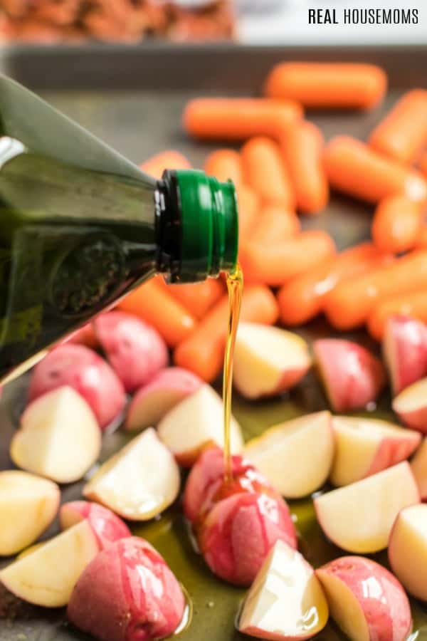 olive oil being drizzled over potatoes and carrots