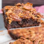 square image of a pecan pie brownie on a spatula over the pan