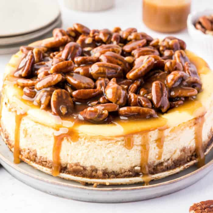square image of a pecan pie cheesecake with caramel sauce dropping down the sides