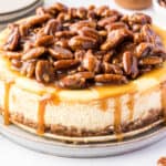 square image of a whole pecan pie cheesecake with caramel sauce dropping down the sides