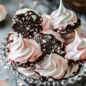 These sweet Peppermint Bark Meringues are made with just a handful of ingredients! They’re adorably festive with candy cane stripes, dipped in dark chocolate, and sprinkled with crushed candy cane pieces!