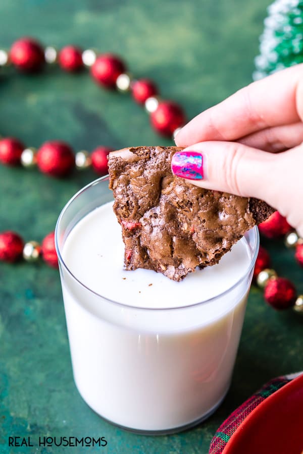 Peppermint Brownie Brittle piece being dunked into a glass of milk
