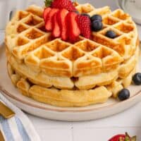three waffles stacked on a plate topped with berries with recipe name at the bottom