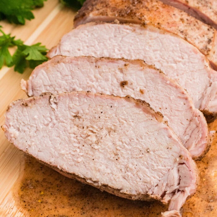 square image of roasted pork loin cut into slices on a cutting board
