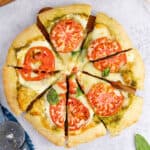 square image of pesto pizza cut into slices on a wooden board