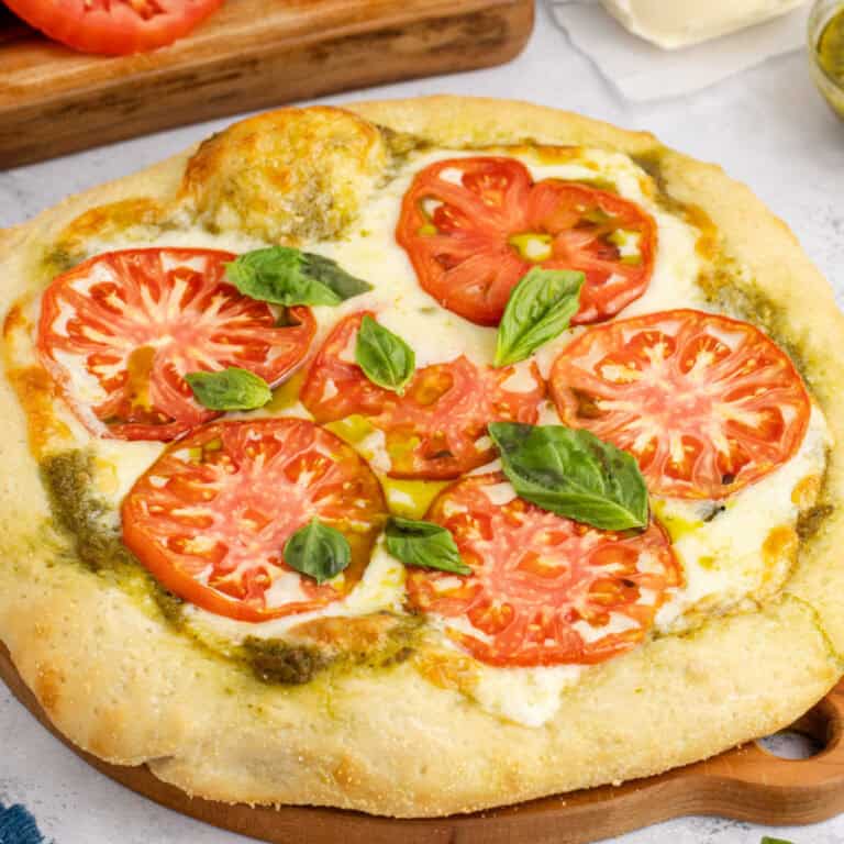 square image of a whole pesto pizza topped with fresh basil leaves on a wooden board