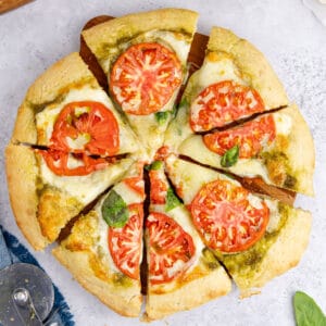 square image of pesto pizza cut into slices on a wooden board