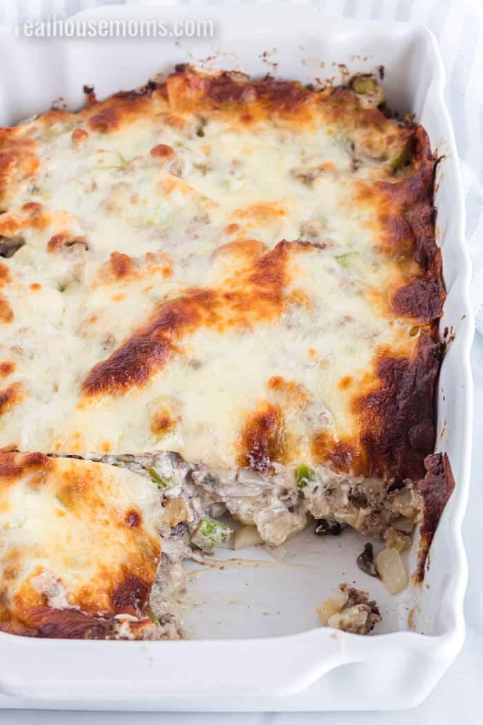 cheesesteak casserole in a baking dish with a piece taken out to show layers