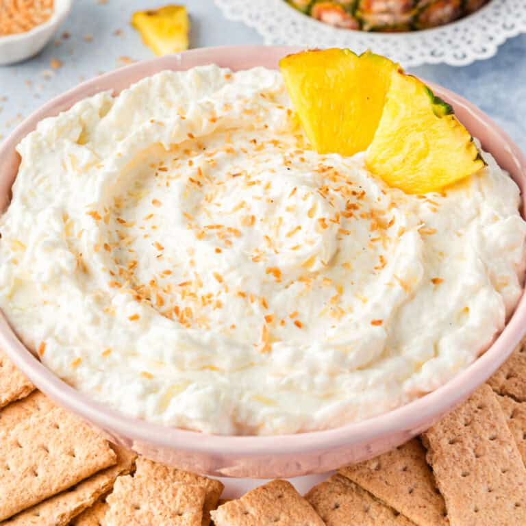 square image of pina colada dip topped with toasted coconut and a two pineapple wedges