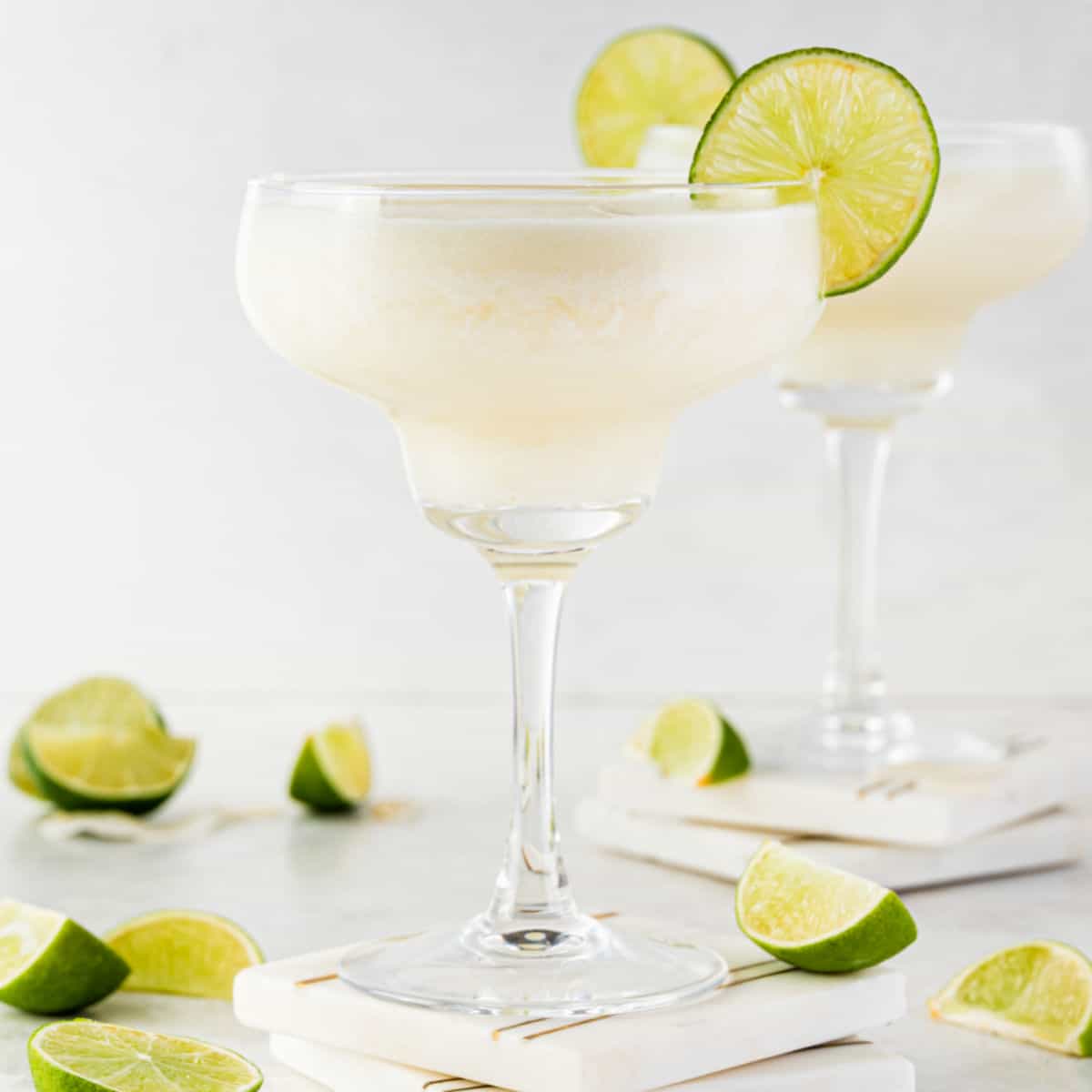 square image of two pina rita coconut pineapple margaritas with lime slices on the rim