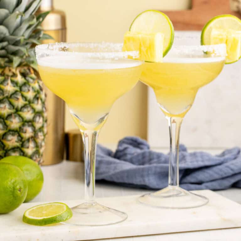square image of pineapple coconut margarita twos pineapple coconut margarita next to a pineapple and lime