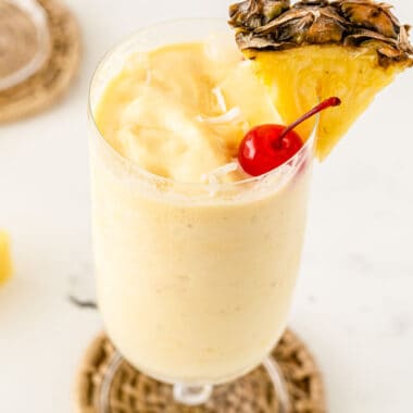 square image of a pineapple rum slushie garnished with a cherry, coconut flakes, and a wedge of pinepple