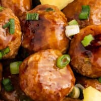 image of pineapple teriyaki turkey meatballs in a serving bowl with green onion and pineapple for garnish with the title of the post on top of the image in pink and black lettering