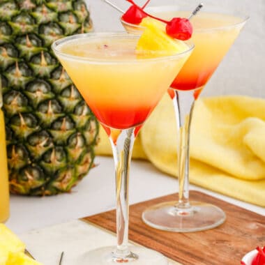 square image of two pineapple upside down cake martinis next to a pineapple