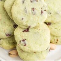 pistachio chip cookies piled up on a plate with recipe name at the bottom