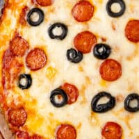 picture of pizza dip topped with mini pepperoni and sliced black olives with blue and black lettering on the top of the image