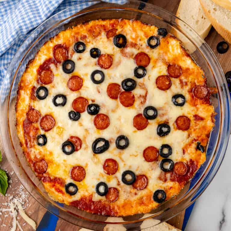 square image of pizza dip topped with mini pepperoni and sliced black olives