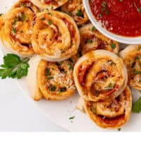 pizza pinwheels arranged on a plate next to a bowl of marinara with recipe name at the bottom