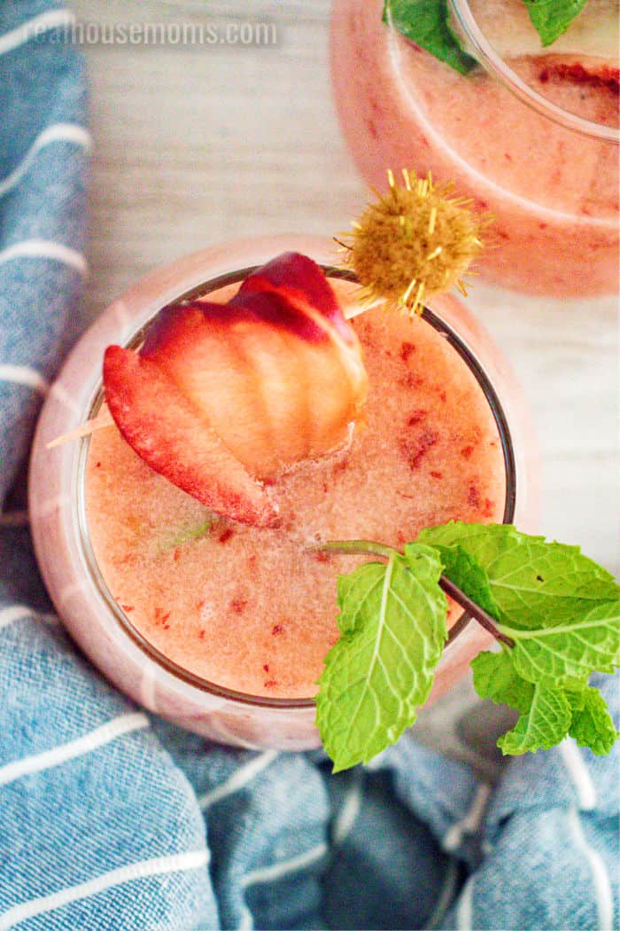 looking down into a glass of frozen peach margarita with fruit and mint for garnish