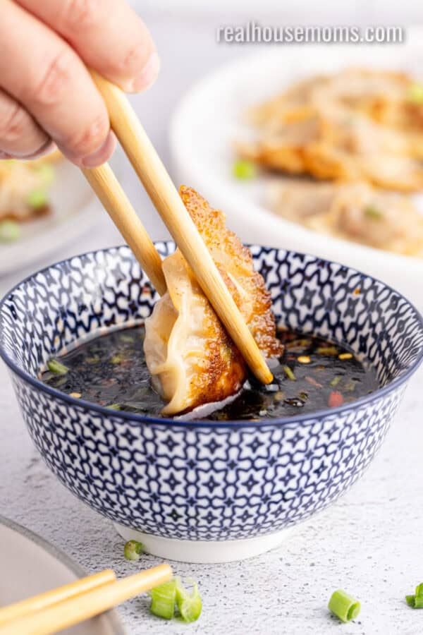 chopstick dipping a potsticker into a bowl of sauce