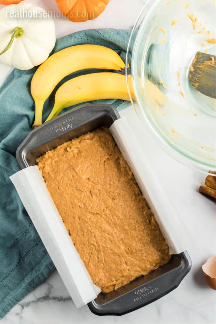 pumpkin banana bread batter in a loaf pan with parchment paper for easy removal after baking