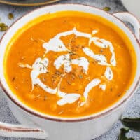 square image of pumpkin & butternut squash soup in a bowl topped with sour cream and thyme