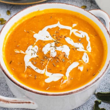 square image of pumpkin & butternut squash soup in a bowl topped with sour cream and thyme