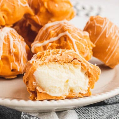 square image of pumpkin cheesecake balls on a plate with one cut in half to show the filling