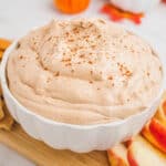 square angled image of pumpkin pie cheesecake dip in a serving bowl on a wooden tray with apple slices