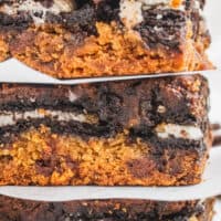 close up image of three pumpkin slutty brownies stacked up with parchment paper pieces in between with the title of the post on top of the image in orange and black lettering