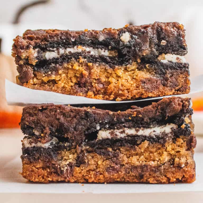 square image of two pumpkin slutty brownies stacked up with parchment paper pieces in between