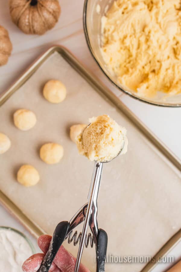 cookie scoop of sugar cookie dough over a lined baking sheet